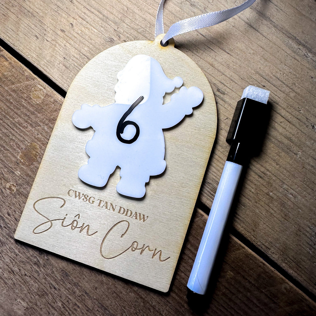 Wooden tag with a white cutout number '6' and a pen on a wooden surface